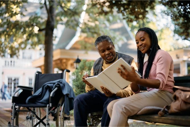 Two people sitting on a bench looking at an open book.