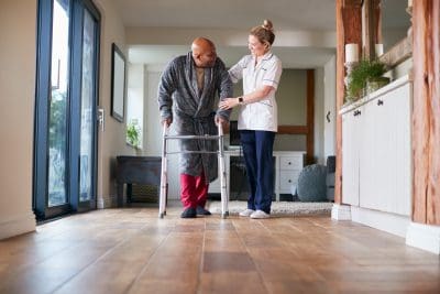 A person with a walker and nurse in the background.