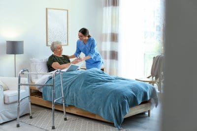 A woman in blue shirt standing next to bed.