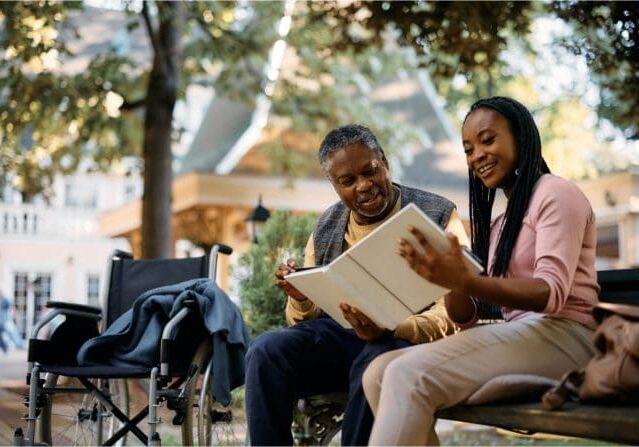 Two people sitting on a bench looking at an open book.